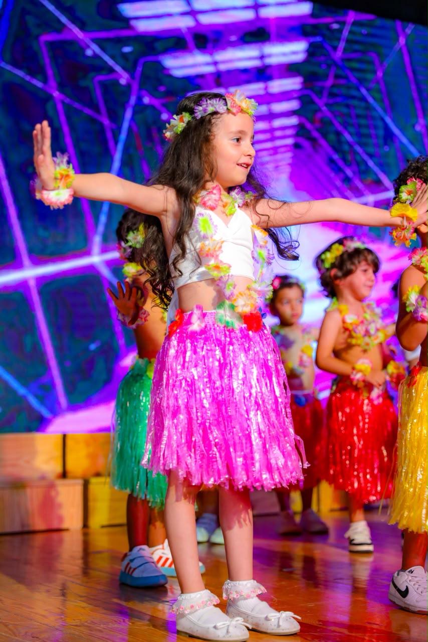 Andy Pandy graduate in pink hula skirt dancing on stage with classmates