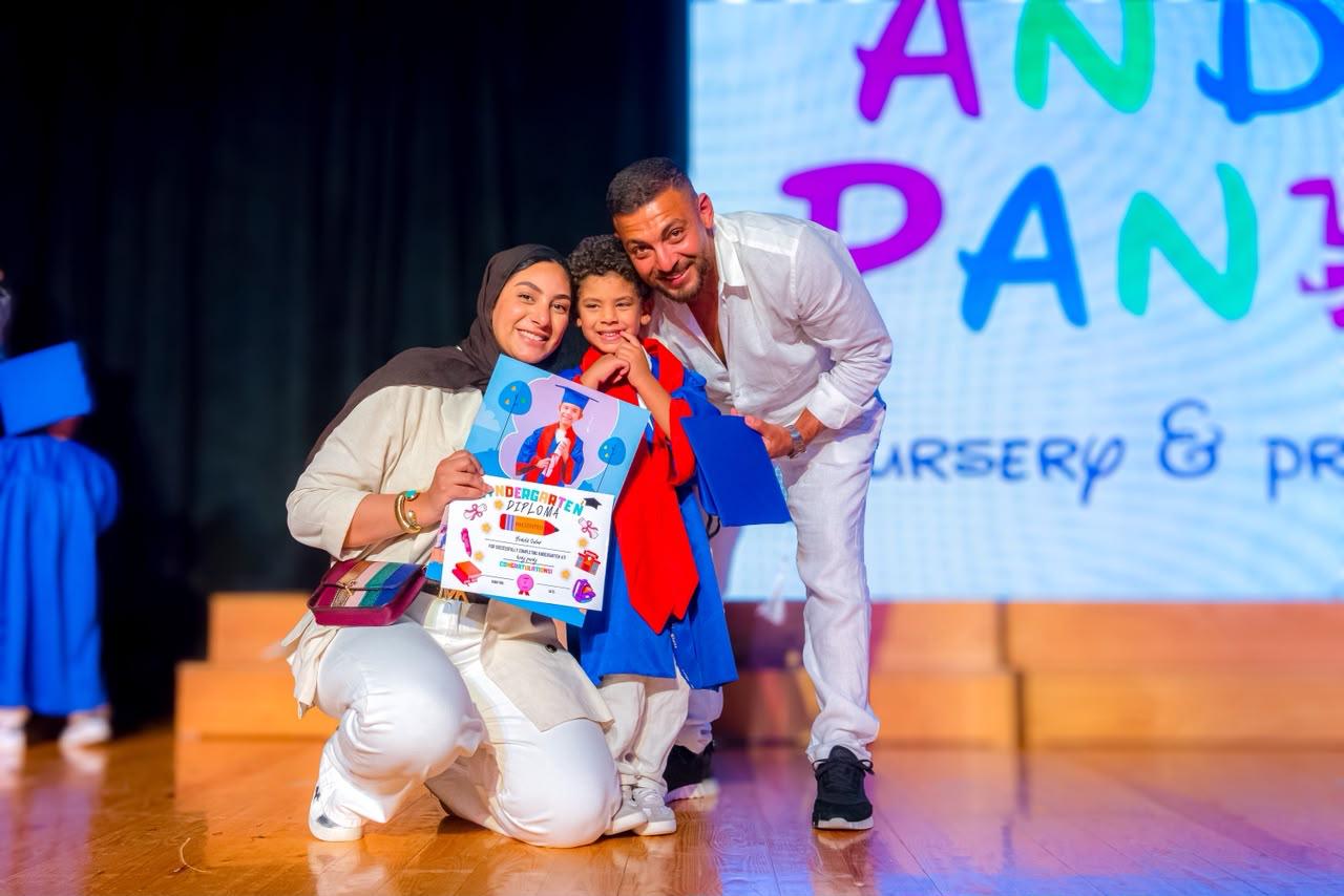 Andy Pandy graduate boy in cap and gown celebrating his diploma with parents on stage