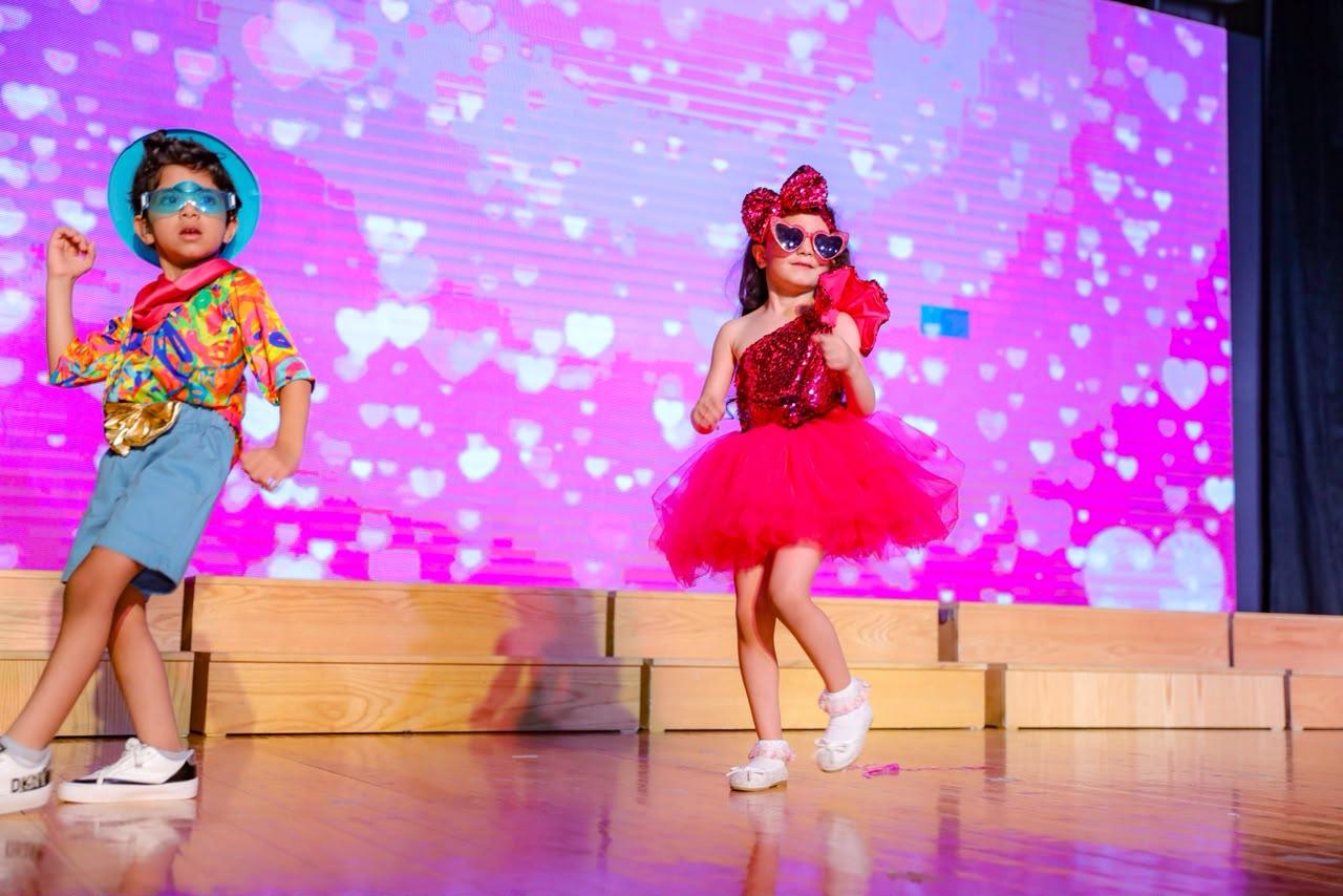 Andy Pandy graduates dancing in vibrant costumes with heart-themed stage backdrop