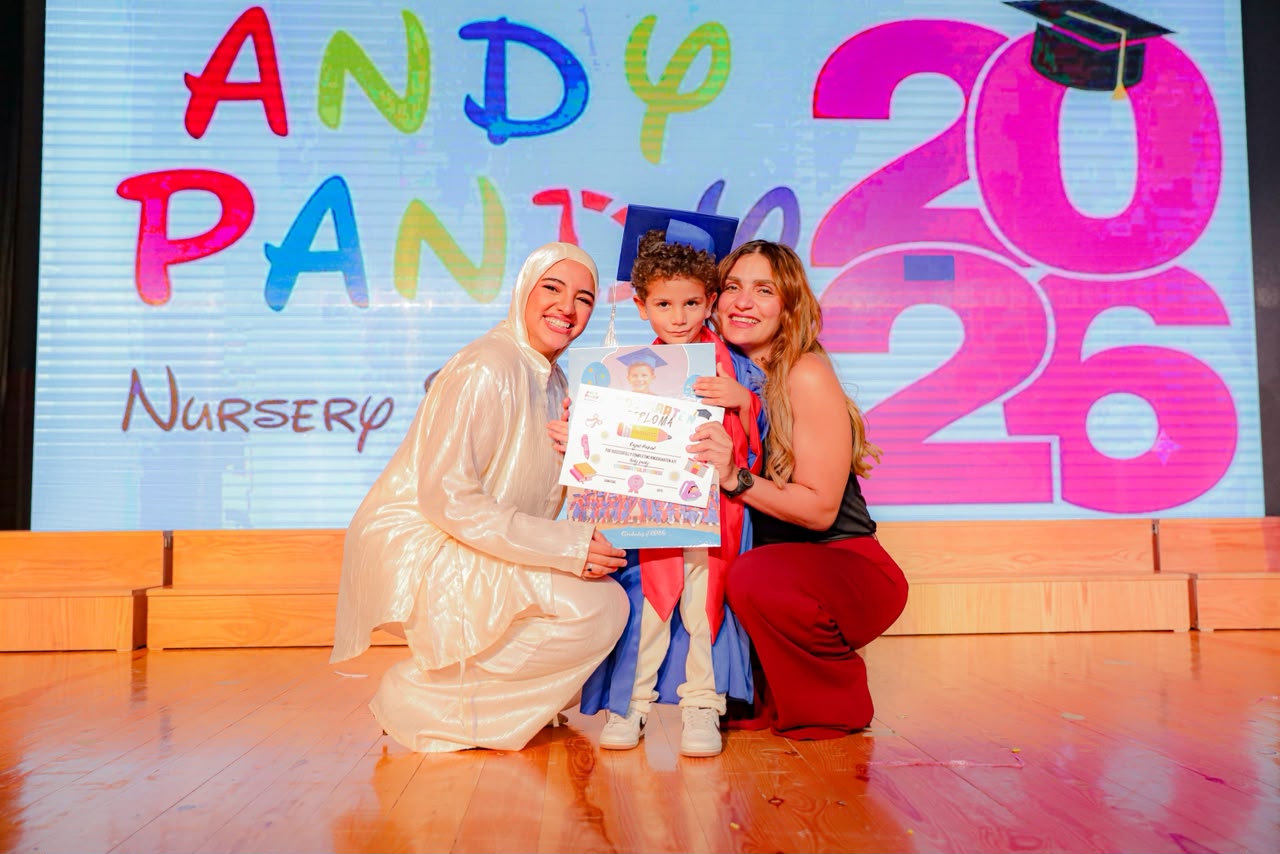 Andy Pandy graduate posing with his diploma between two teachers in front of the Andy Pandy 2026 backdrop