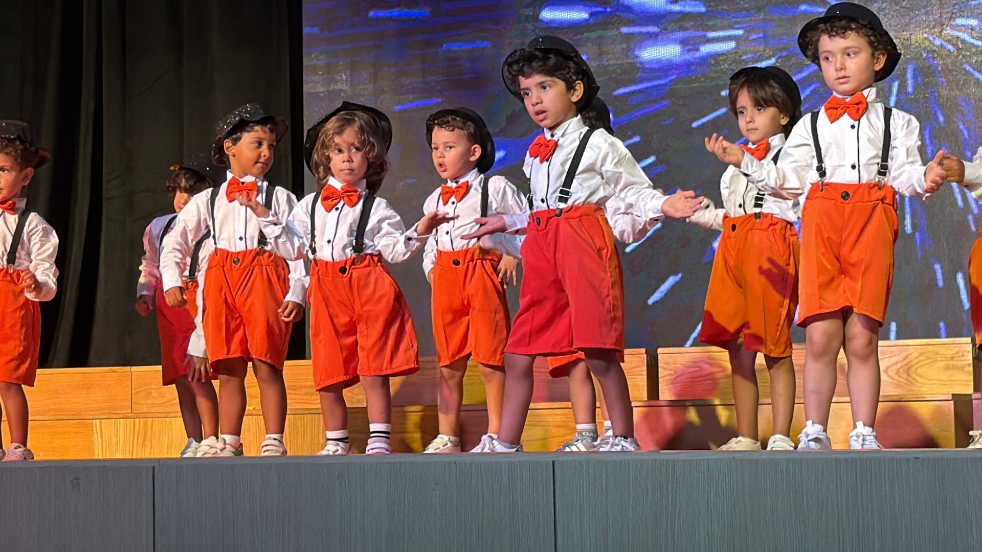 Andy Pandy graduates in white shirts, red bowties and orange shorts performing on stage