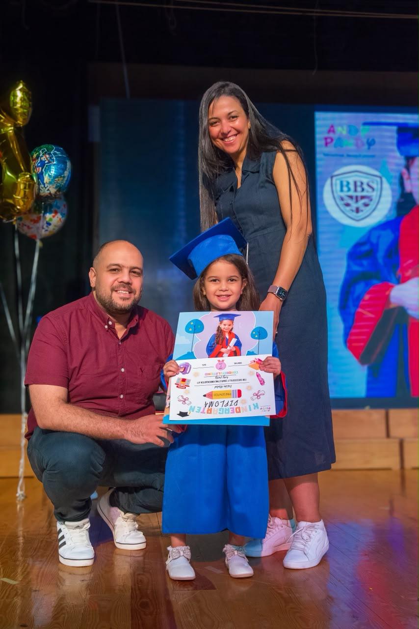 Andy Pandy graduate holding her Kindergarten Diploma with proud parents on stage