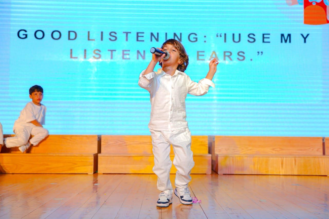 Andy Pandy graduate singing into a microphone on stage with 'good listening' backdrop